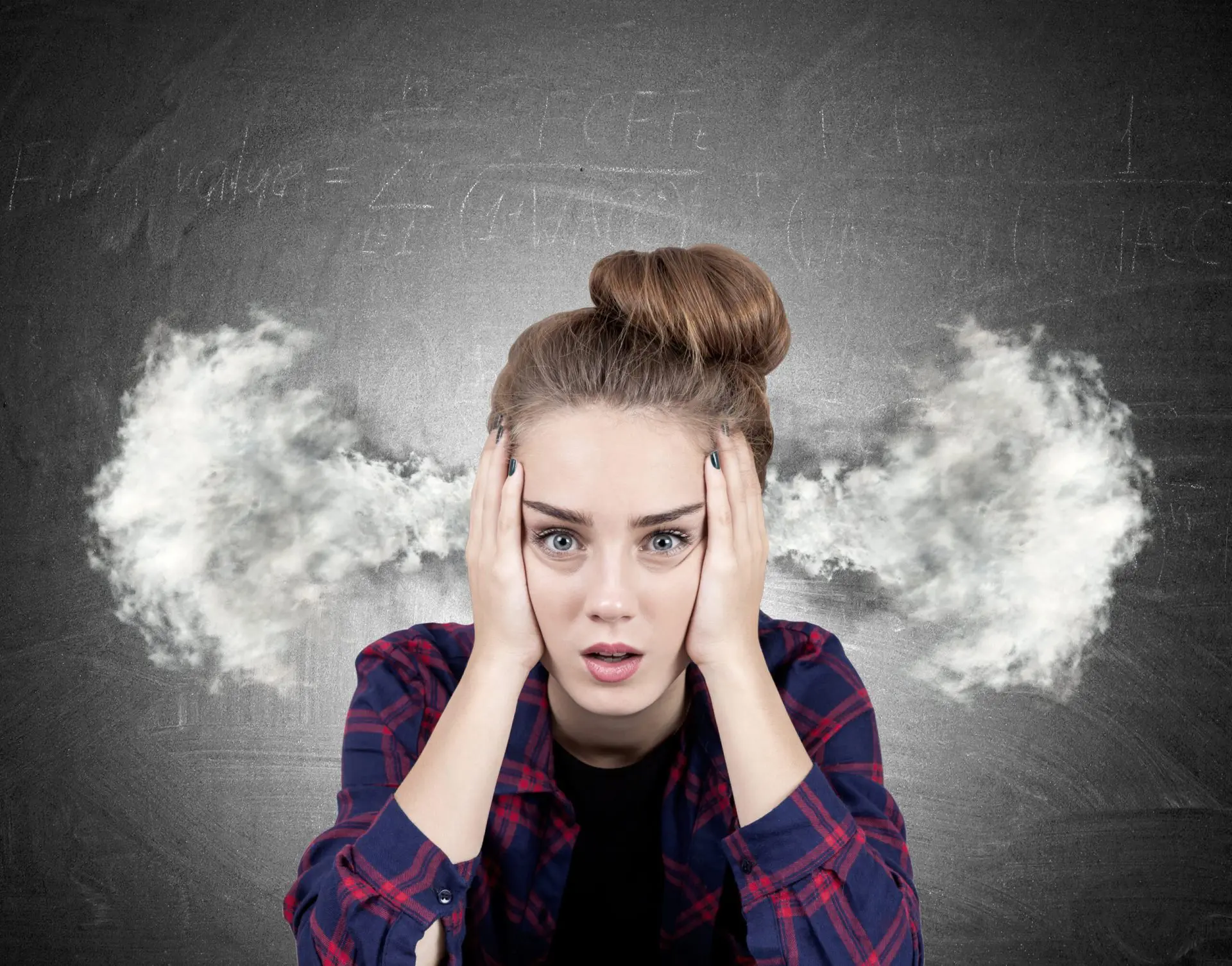 Close up portrait of an angry teenage girl wearing a red checkered shirt and sitting near a blackboard. Steam is going out of her ears.